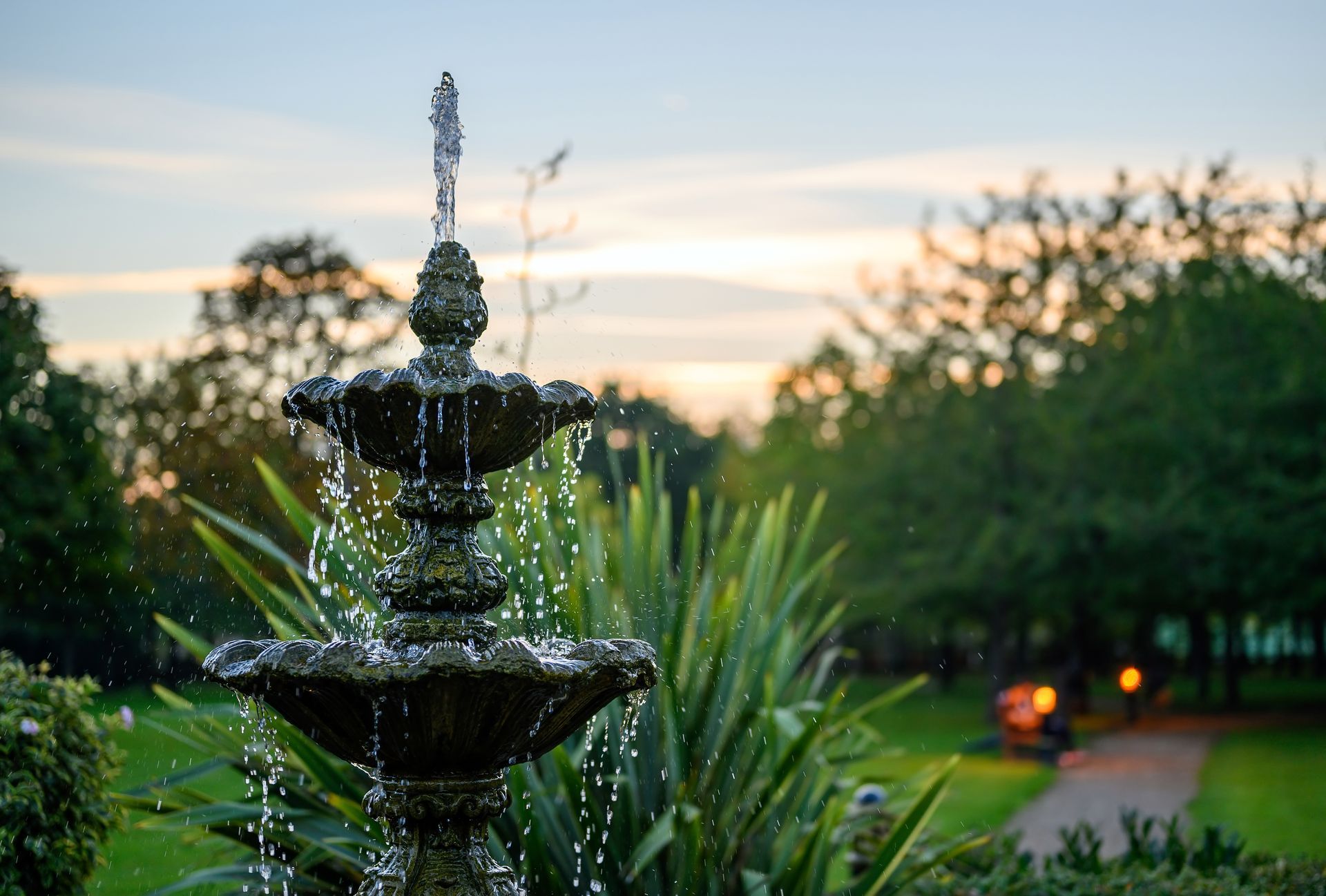 a fountain in a garden with a sunset in the background a fountain in a garden with a sunset in the background