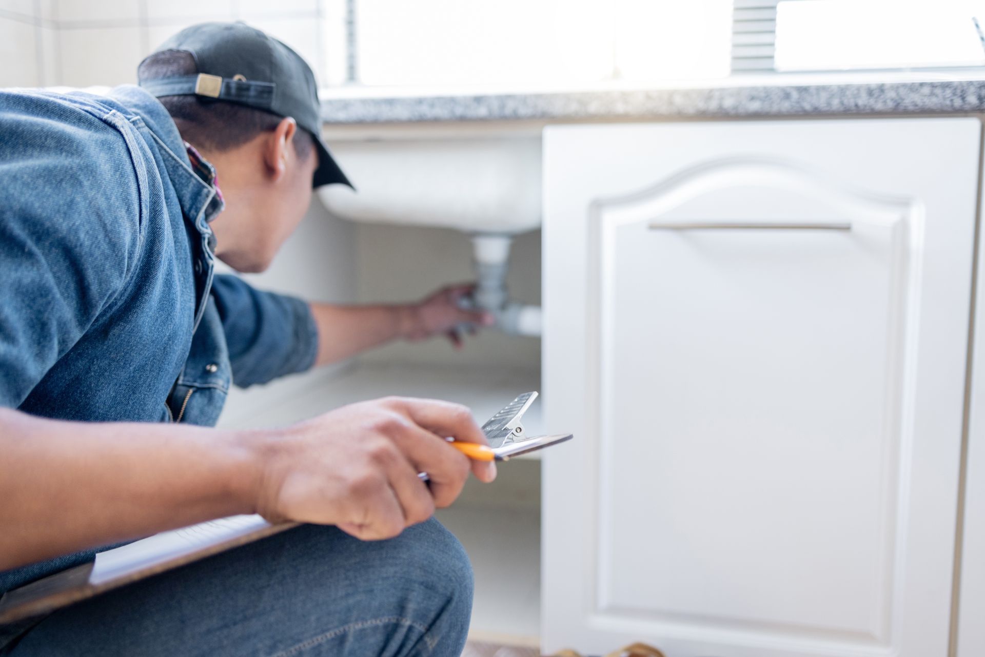 a man is working on a sink while holding a wrench and a clipboard a man is working on a sink while holding a wrench and a clipboard
