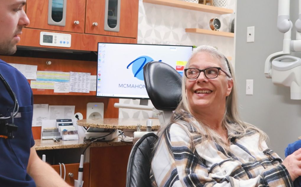 Woman looking in a mirror, happy with her cosmetic results from McMahon Dental.