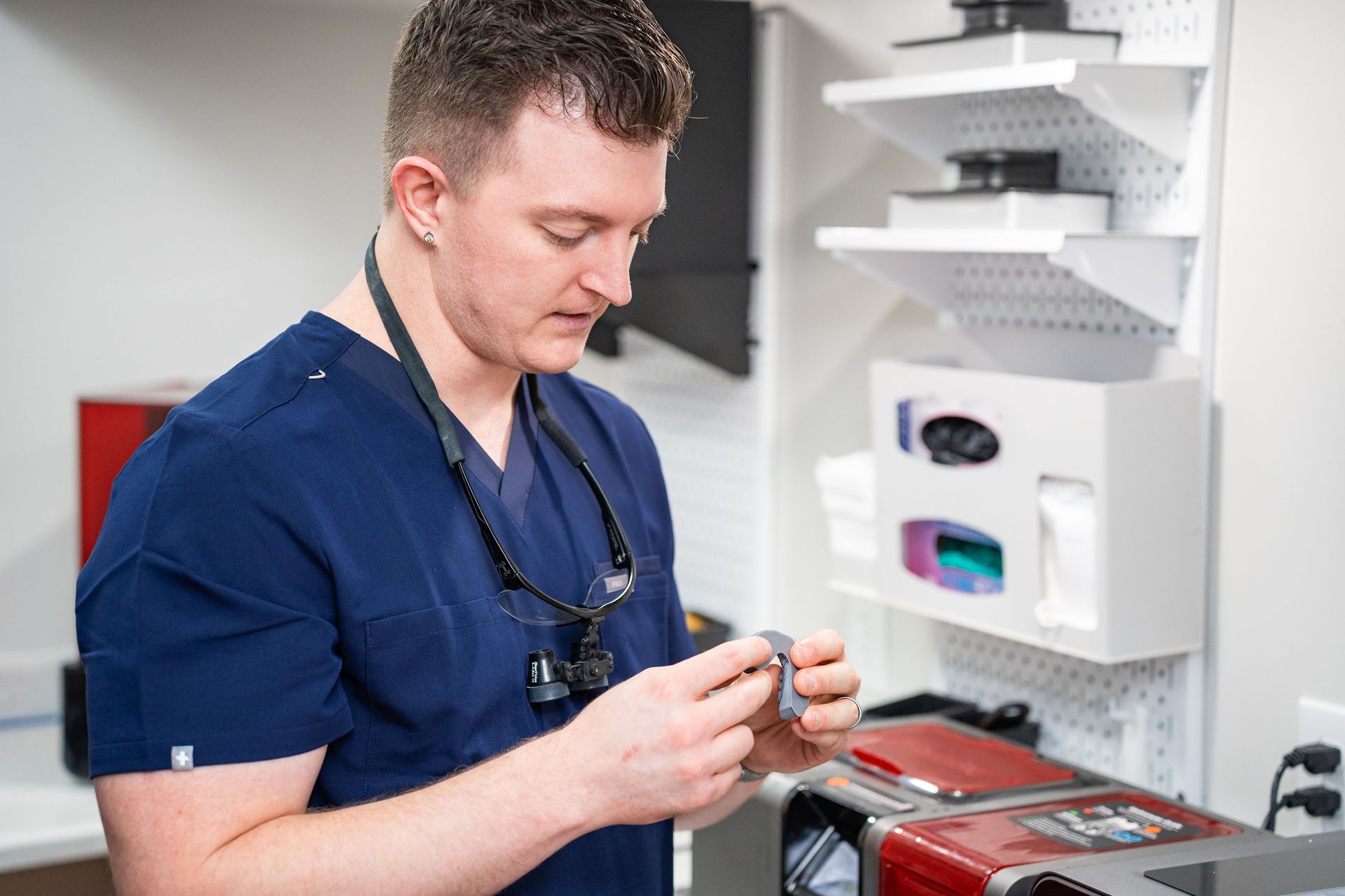 McMahon Dental's technician in blue scrubs inspecting a dental crown in their dental lab.