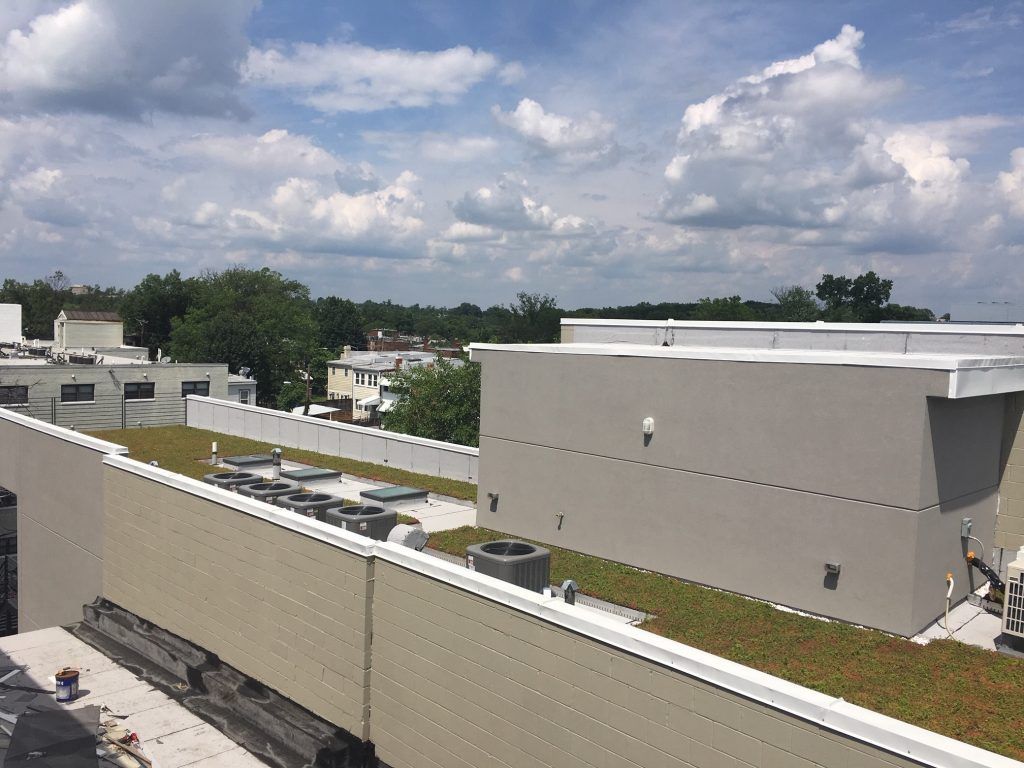 Rooftop view of commercial buildings with green roofs, HVAC units, and a cloudy blue sky.