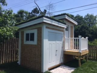 A small, white shed with a green roof and wooden deck.