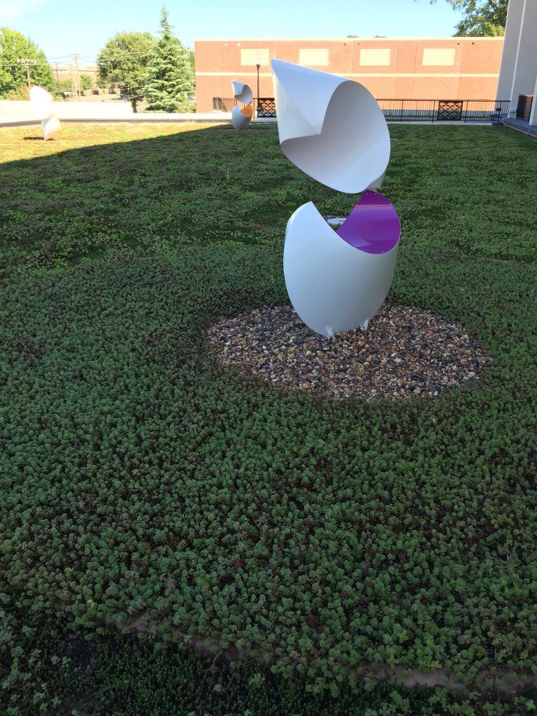 White, open egg-shaped sculpture with purple interior, set on a green roof, sunny day.