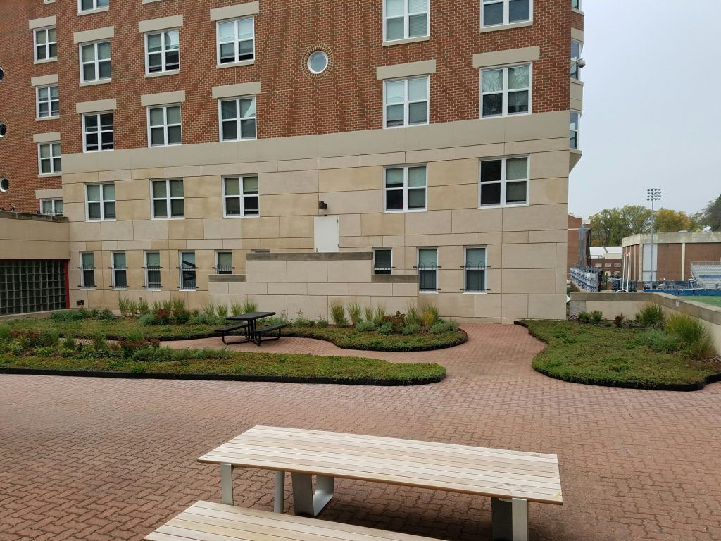 Brick patio with picnic tables, small garden beds, and building with windows.