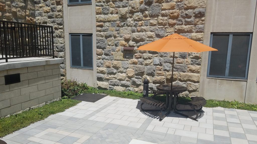Patio with umbrella, small table, and two chairs near a stone building.
