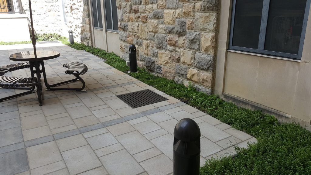 Outdoor patio with stone wall, table, and hedges.