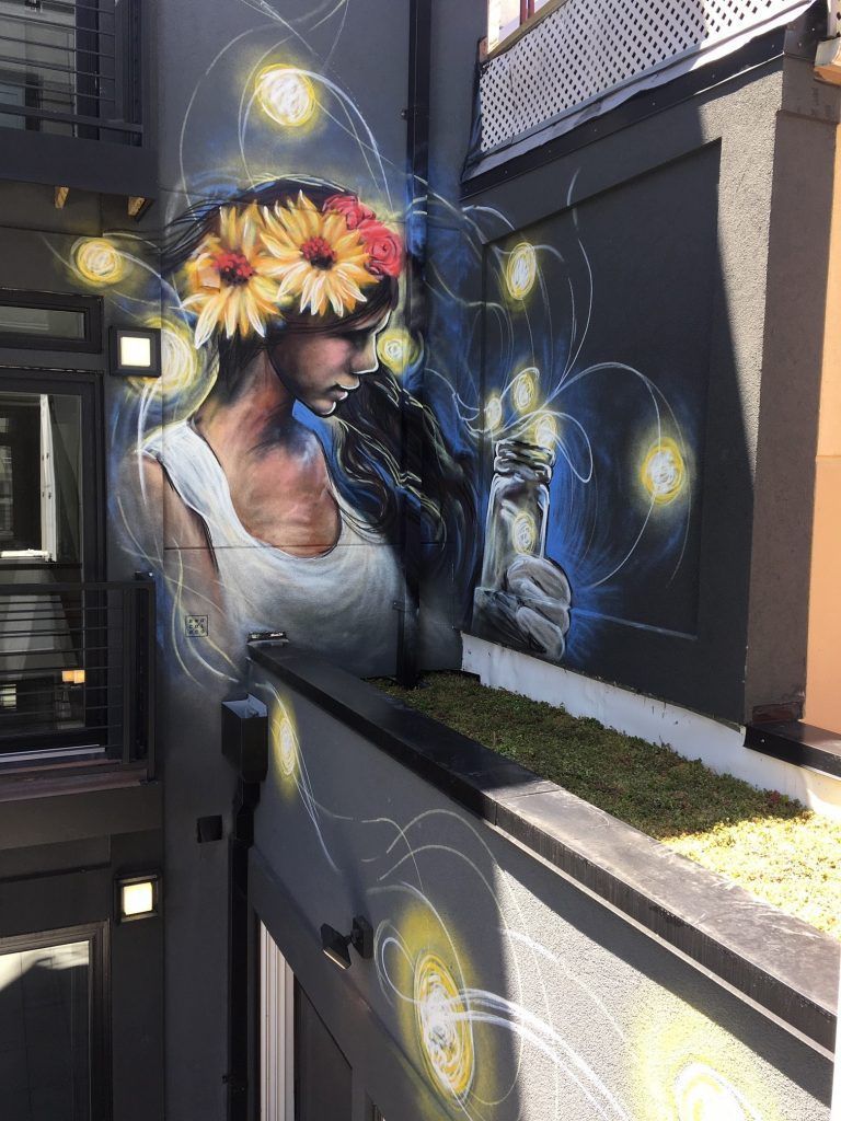 Mural of woman with sunflower crown, reaching for glowing orb.  Gray walls.
