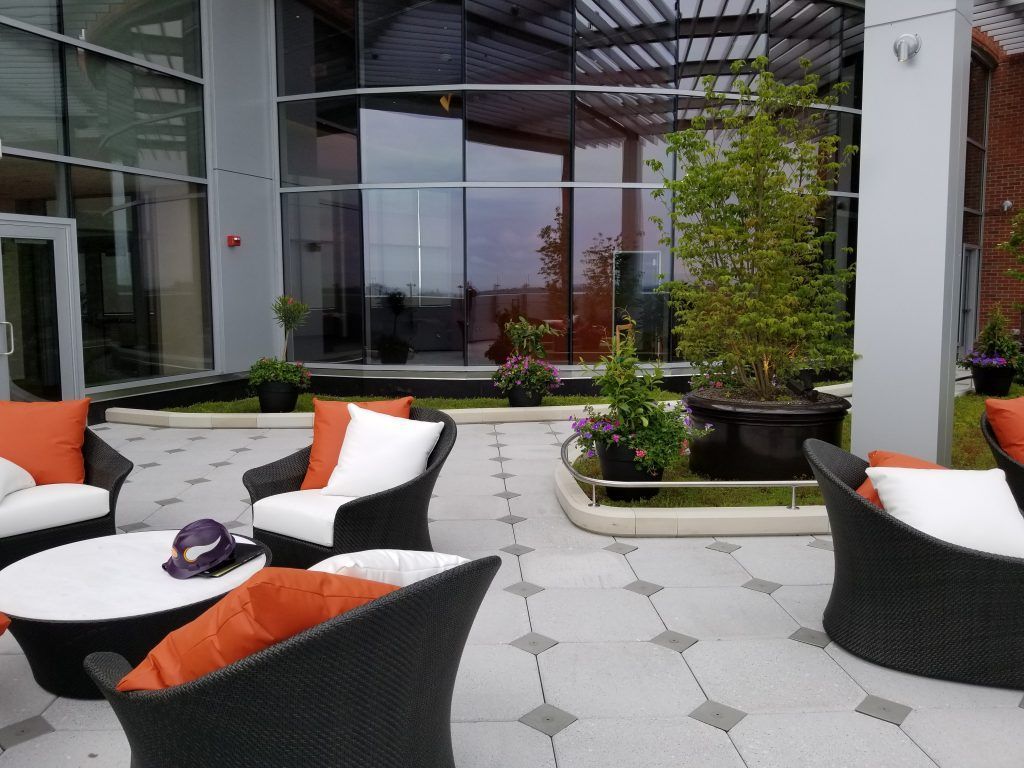 Patio seating with wicker chairs, orange cushions, and a round coffee table on a tiled surface near a modern building.