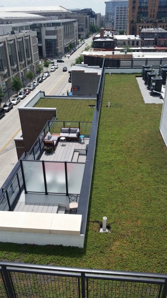 View of a green rooftop with outdoor seating, near a city street. Buildings line the street.