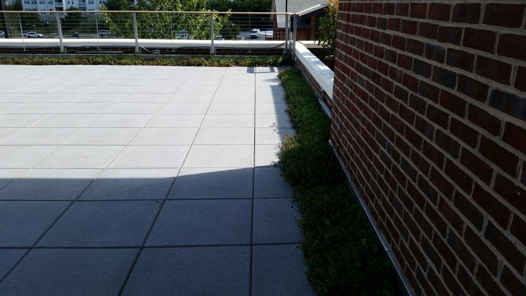 Rooftop patio with gray tiles, brick wall, and green plants along the edge.