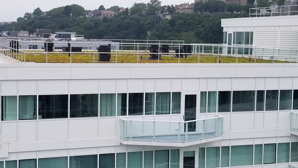 White building with a green roof, glass balconies, and windows overlooking a city skyline.