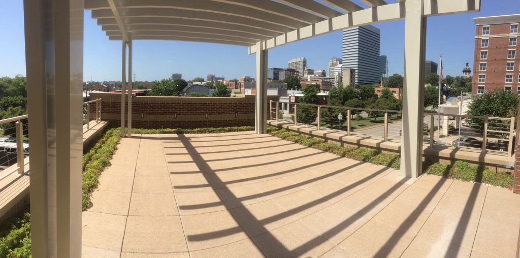 Rooftop patio with cityscape view, featuring a pergola, light-colored pavers, and green shrubbery.