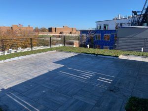 Outdoor paved patio with a black metal fence, grass strip, and construction in the background.
