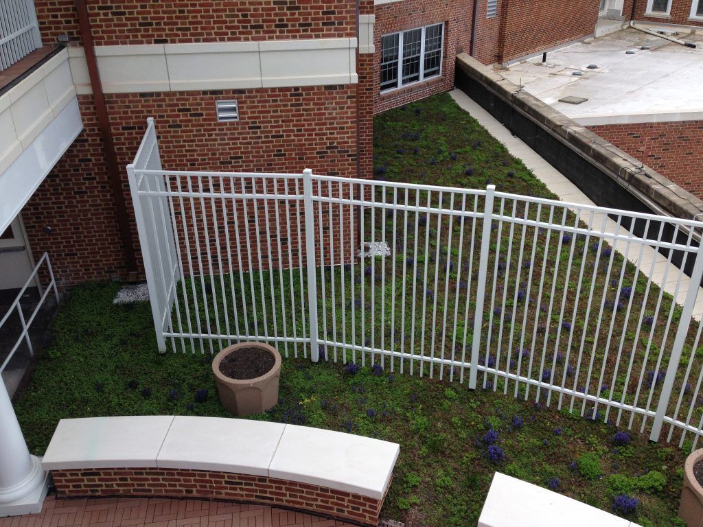 White fence surrounds a small green space next to a brick building.