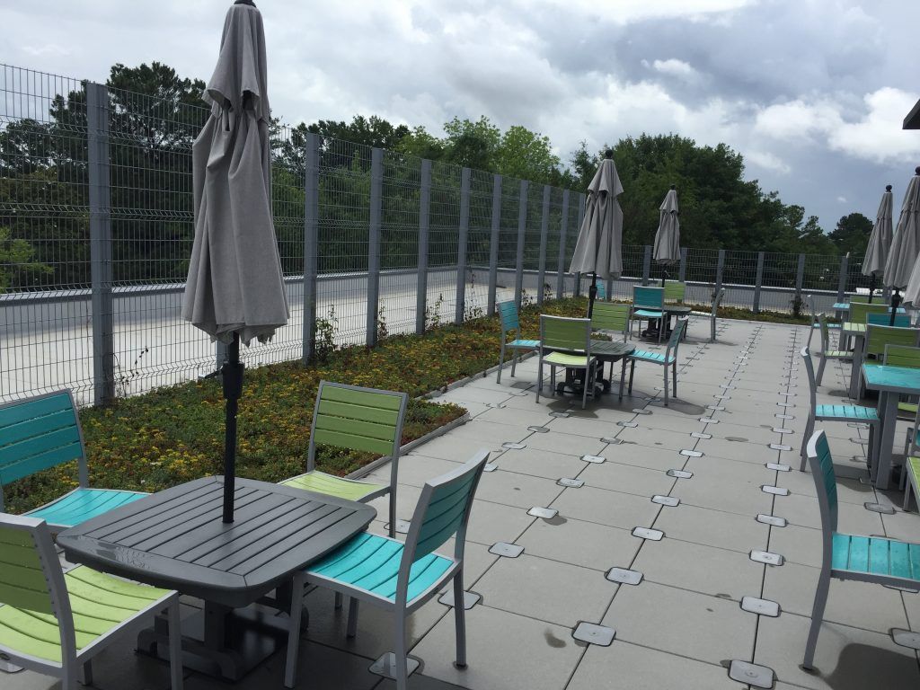 Outdoor dining area with tables, chairs, and umbrellas on a rooftop patio, gray and blue color scheme, cloudy sky.