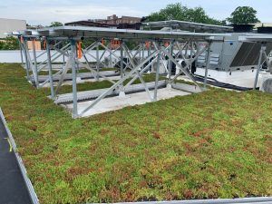 Green roof with solar panels on a rooftop. Metal supports and equipment are visible.