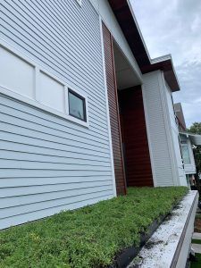 Light blue siding on a modern building, brown wood accents, a green rooftop garden, and a cloudy sky.