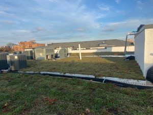 A rooftop with HVAC units, a grassy area, and a blue sky.