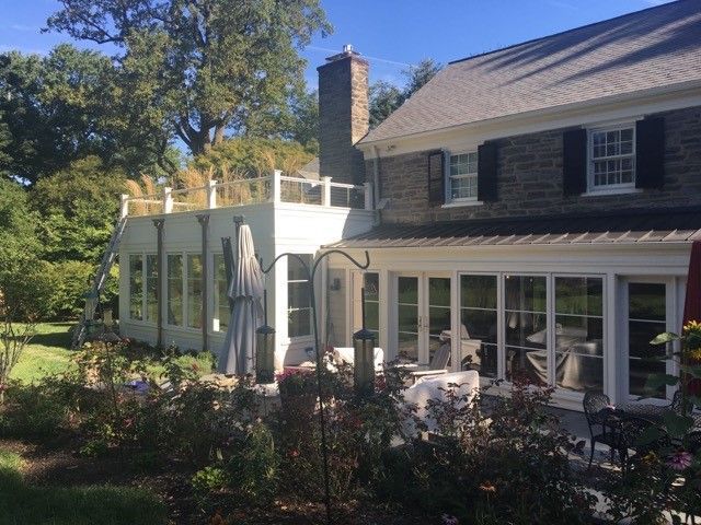 Exterior of a two-story house with a sunroom and deck. White trim, stone facade, and garden in foreground.