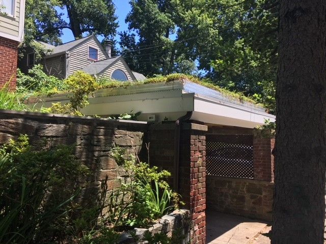 A stone and brick structure with a green roof, set amongst trees, under a blue sky.