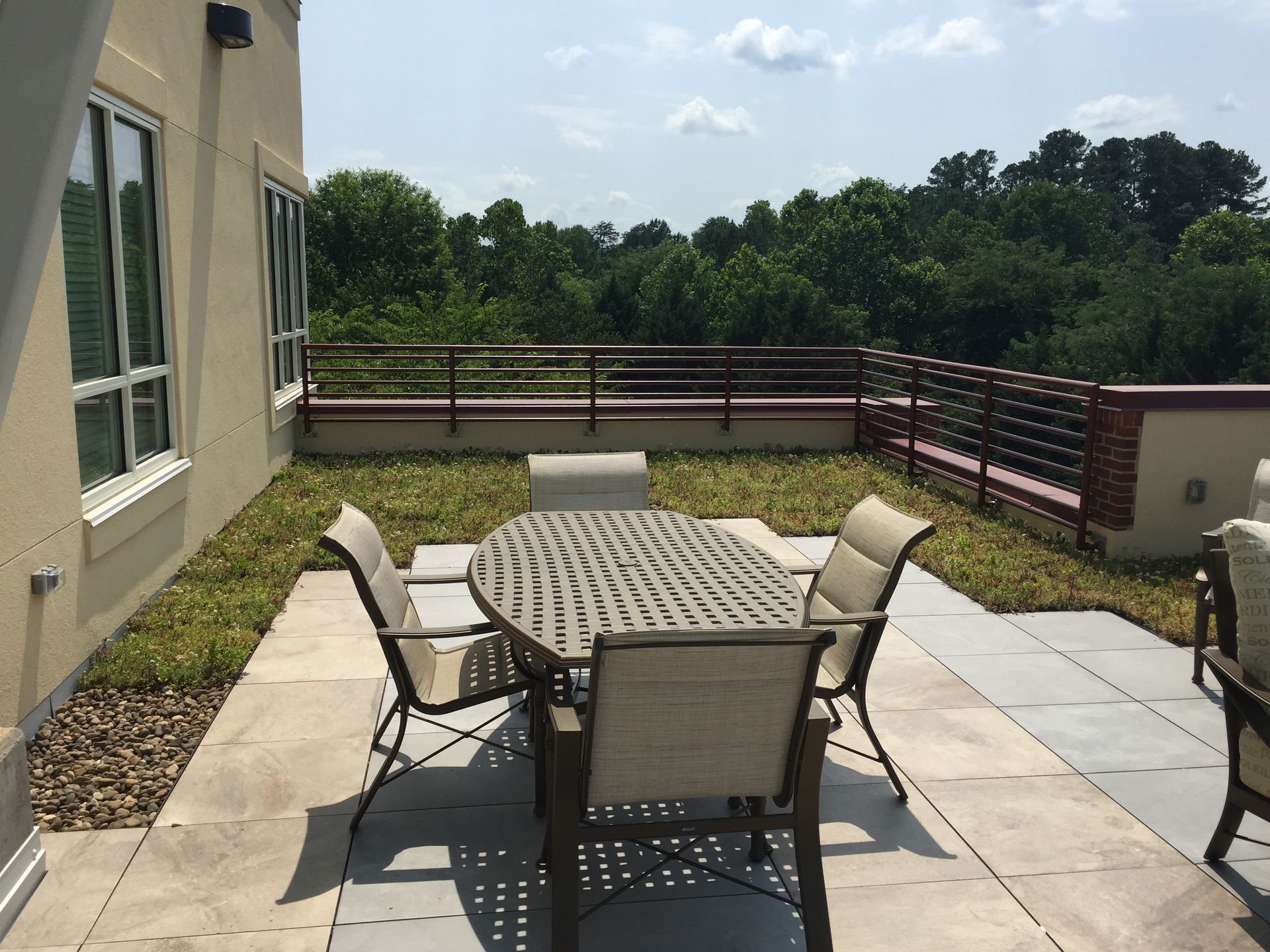 Patio with table, chairs, greenery, and view of trees and sky.