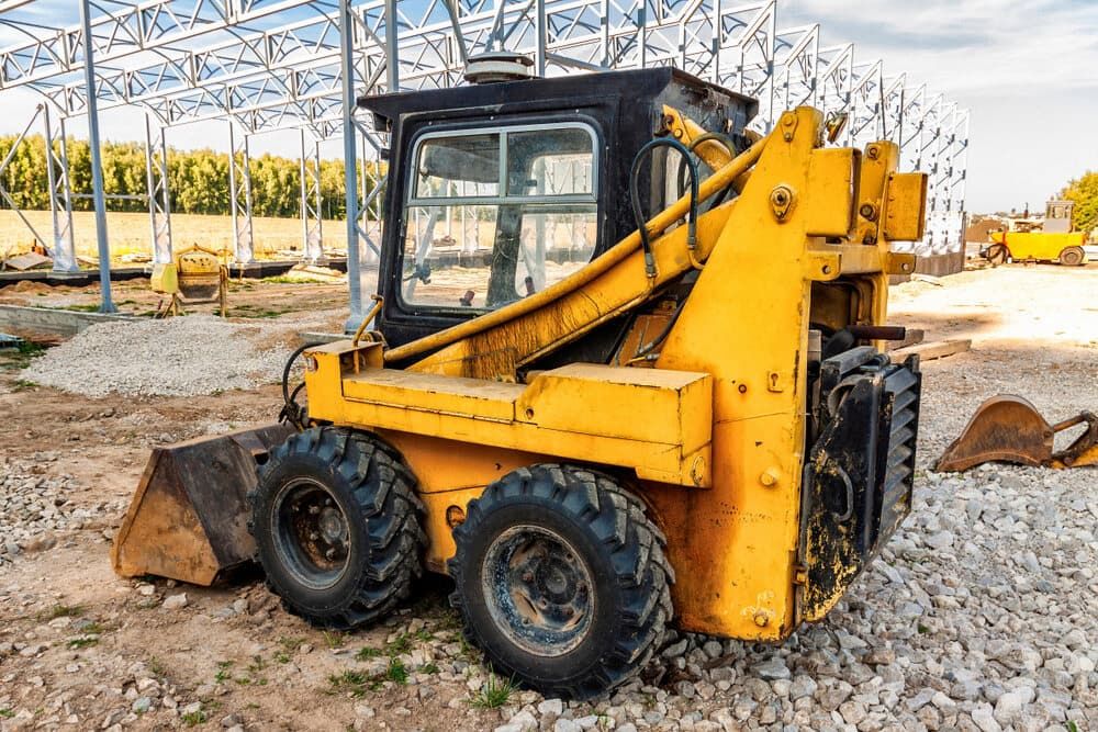 A Small Yellow Bulldozer is Parked in a Gravel Lot at a Construction Site — Simon Dickson Excavations in Mittagong, NSW