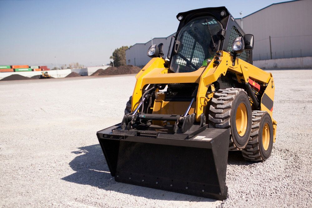 A Yellow Tractor with a Black Bucket is Parked in a Gravel Lot — Simon Dickson Excavations in Moss Vale, NSW