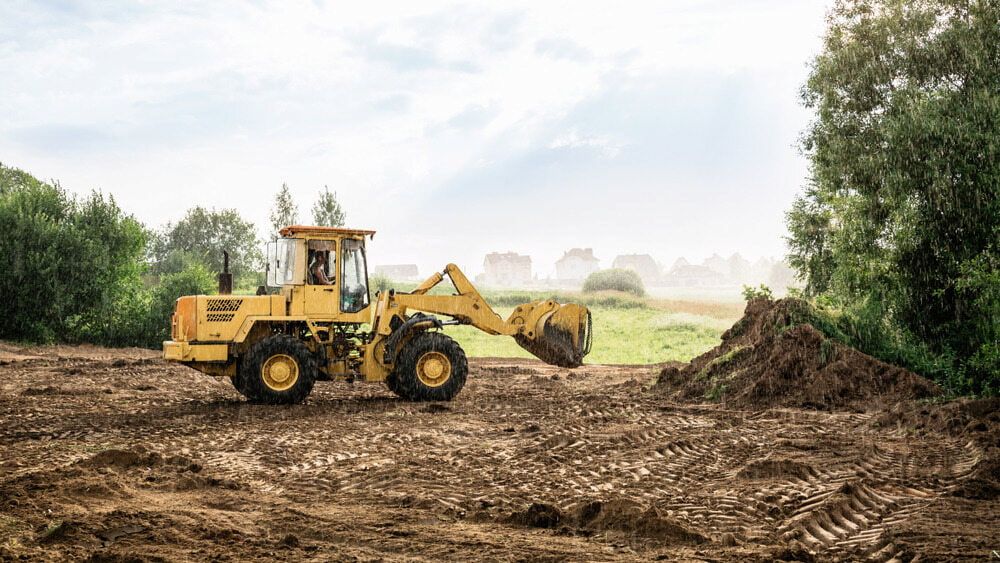 A Yellow Bulldozer is Moving Dirt in a Field — Simon Dickson Excavations in Goulburn, NSW