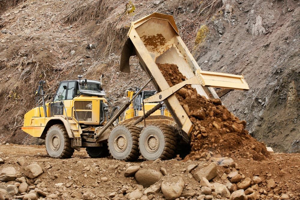 A Dump Truck is Dumping Dirt Into a Pile of Rocks — Simon Dickson Excavations in Moss Vale, NSW