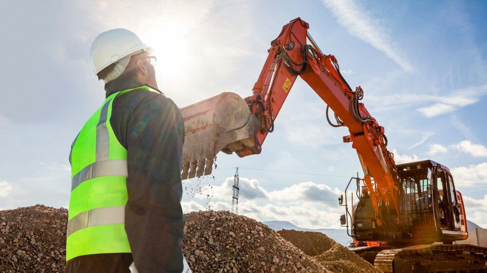A Construction Worker is Standing in Front of an Excavator — Simon Dickson Excavations in Moss Vale, NSW