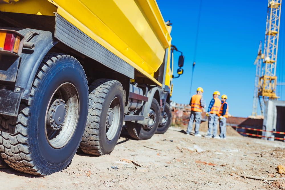 A Group of Construction Workers Are Standing Next to a Yellow Dump Truck — Simon Dickson Excavations in Mittagong, NSW
