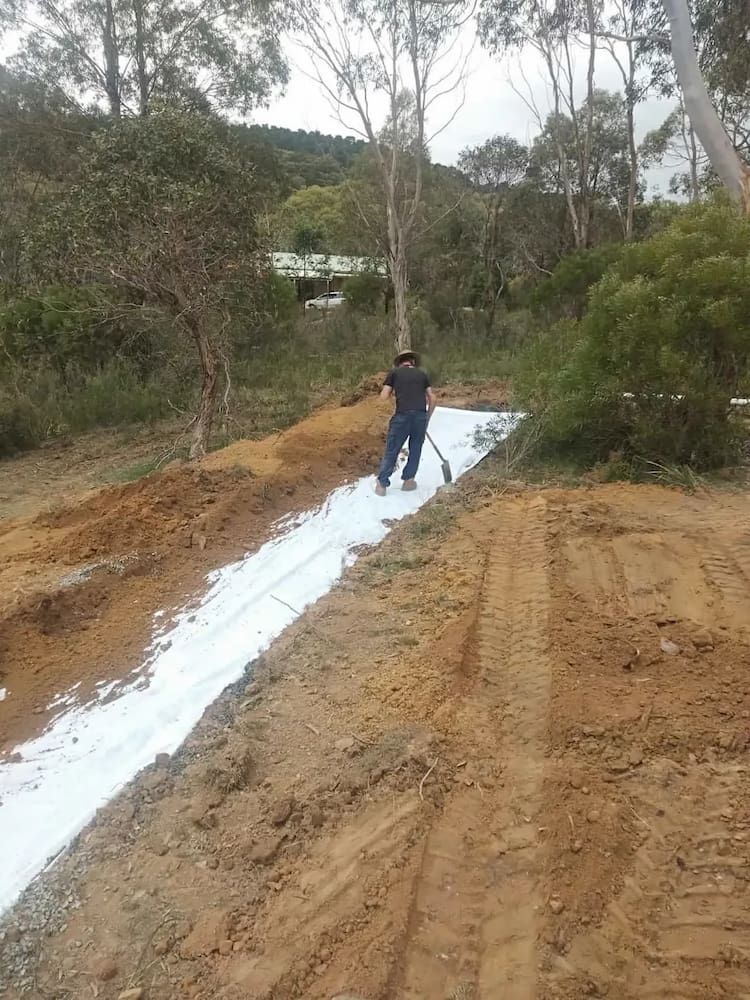 A Man is Laying a White Tarp on a Dirt Road — Simon Dickson Excavations in Moss Vale, NSW