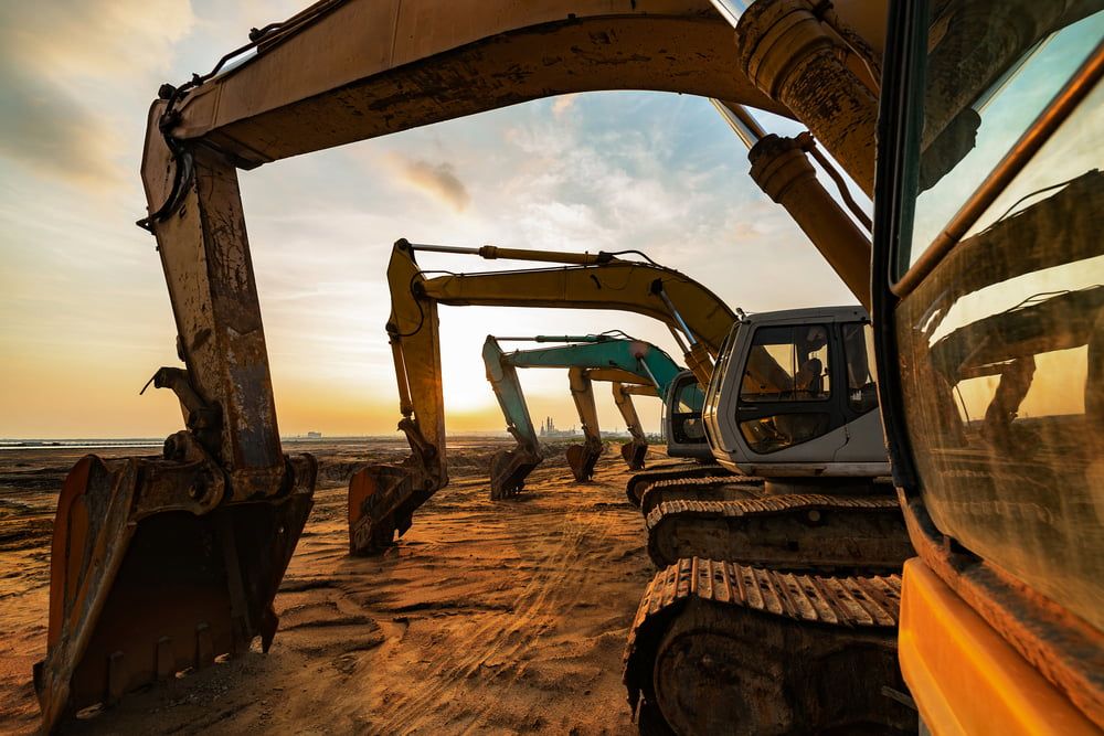 A Row of Excavators Are Parked on a Construction Site at Sunset — Simon Dickson Excavations in Moss Vale, NSW