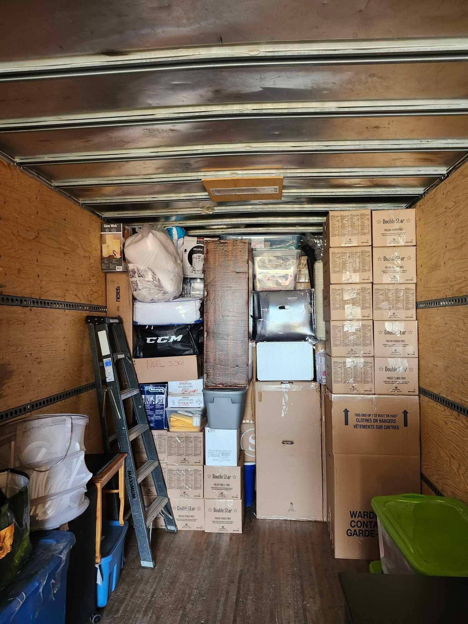 Intérieur d'un camion de déménagement rempli de cartons, d'une échelle et d'objets divers.