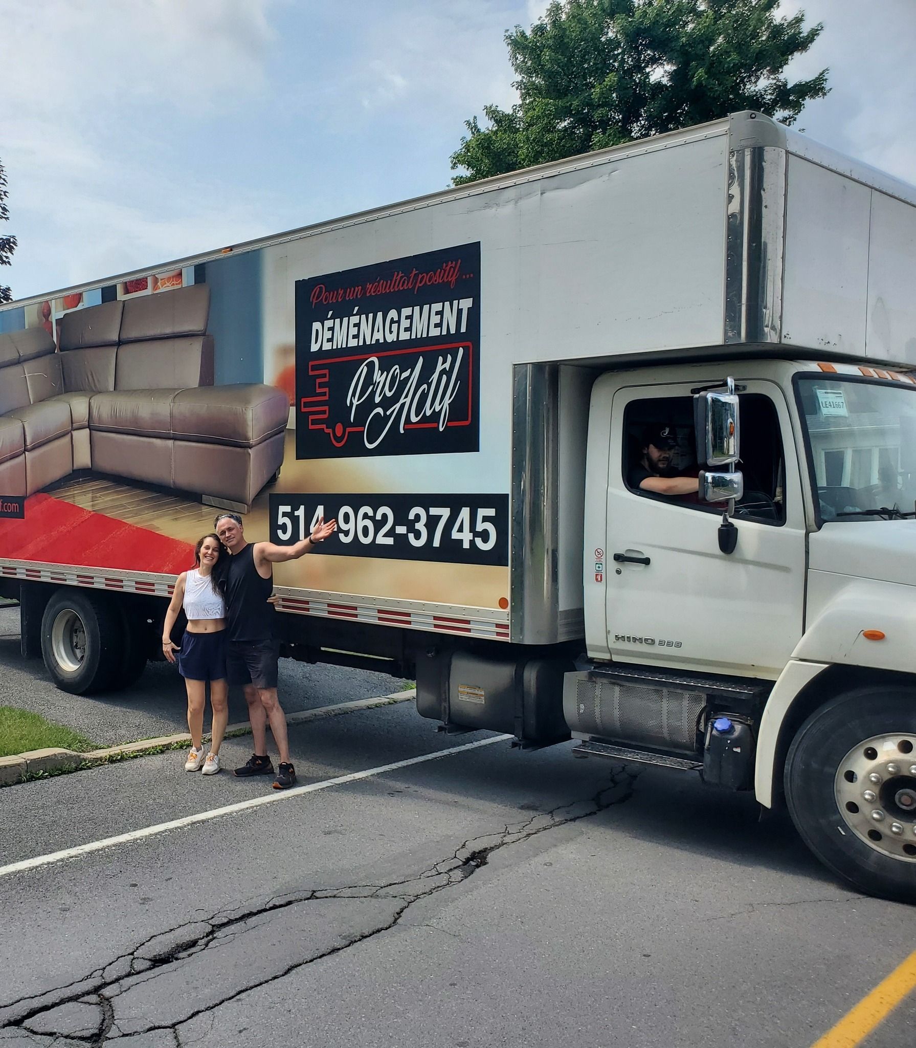 Un couple se tient à côté d'un camion de déménagement portant le logo et le numéro de téléphone de l'entreprise.
