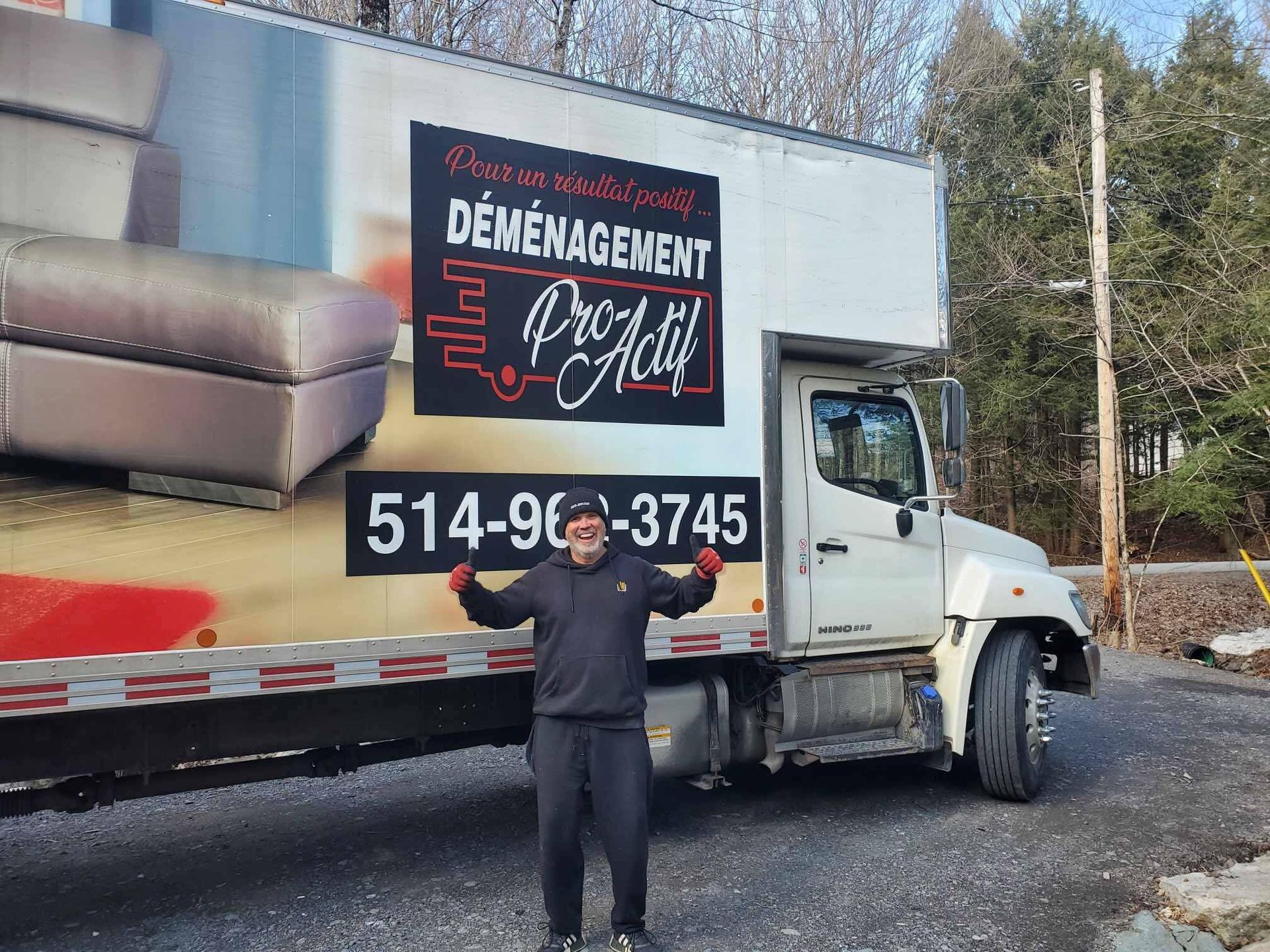 Un homme se tient devant un camion en mouvement portant le nom de l'entreprise, « Déménagement Pro-Actif », et un numéro de téléphone.