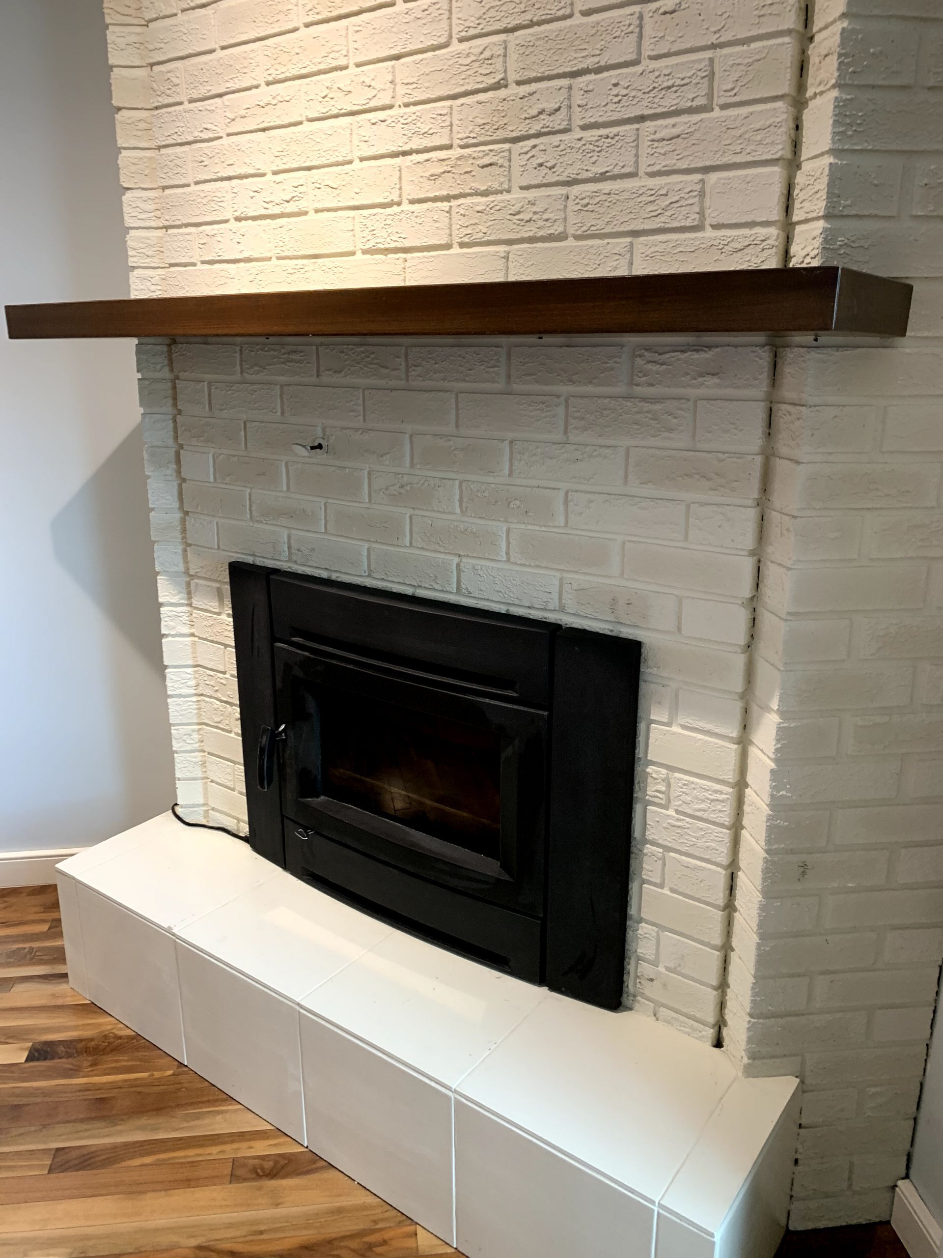 A white brick fireplace with a wooden mantle in a living room.