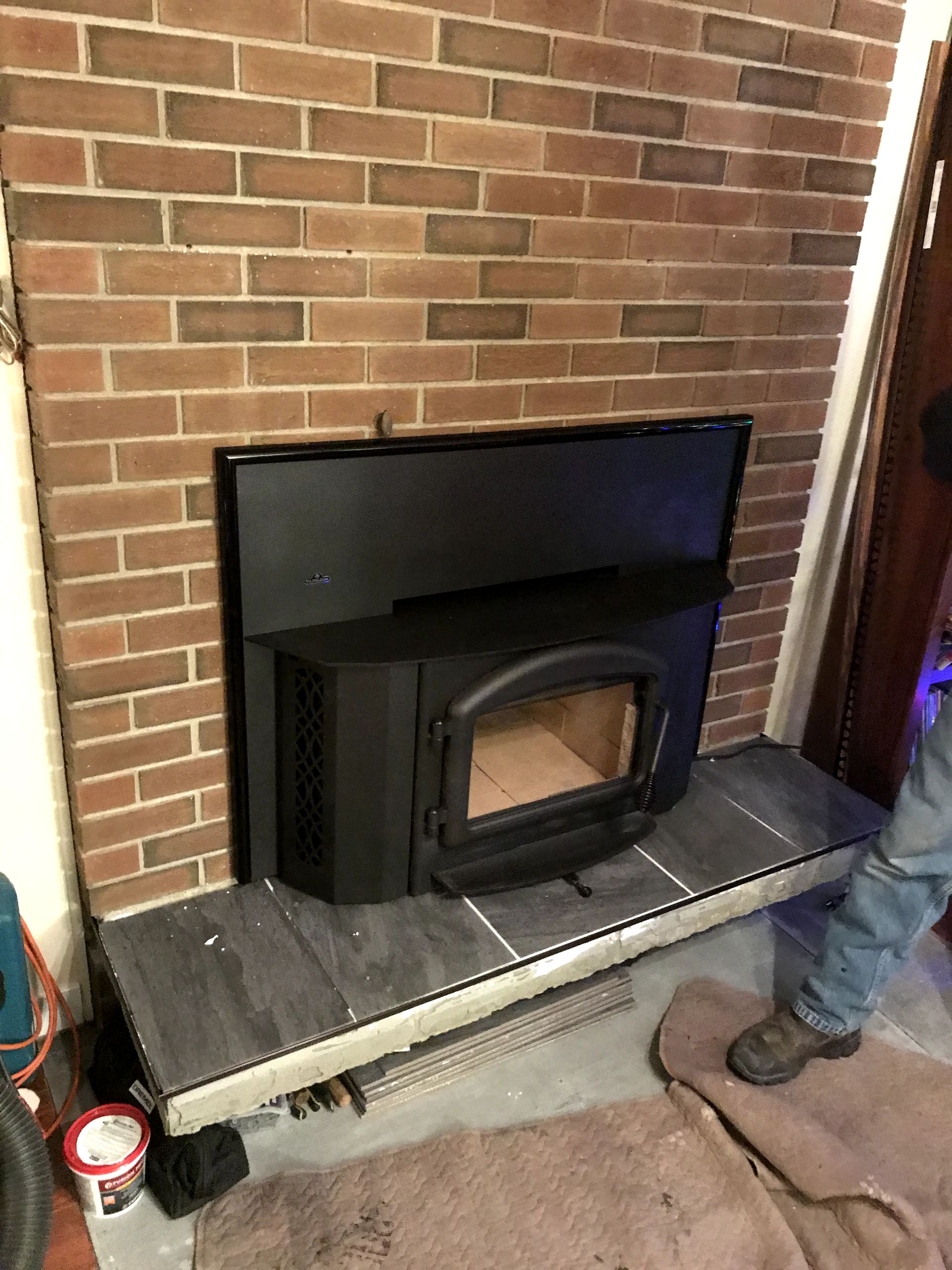 A man is standing next to a fireplace with a wood stove in it.