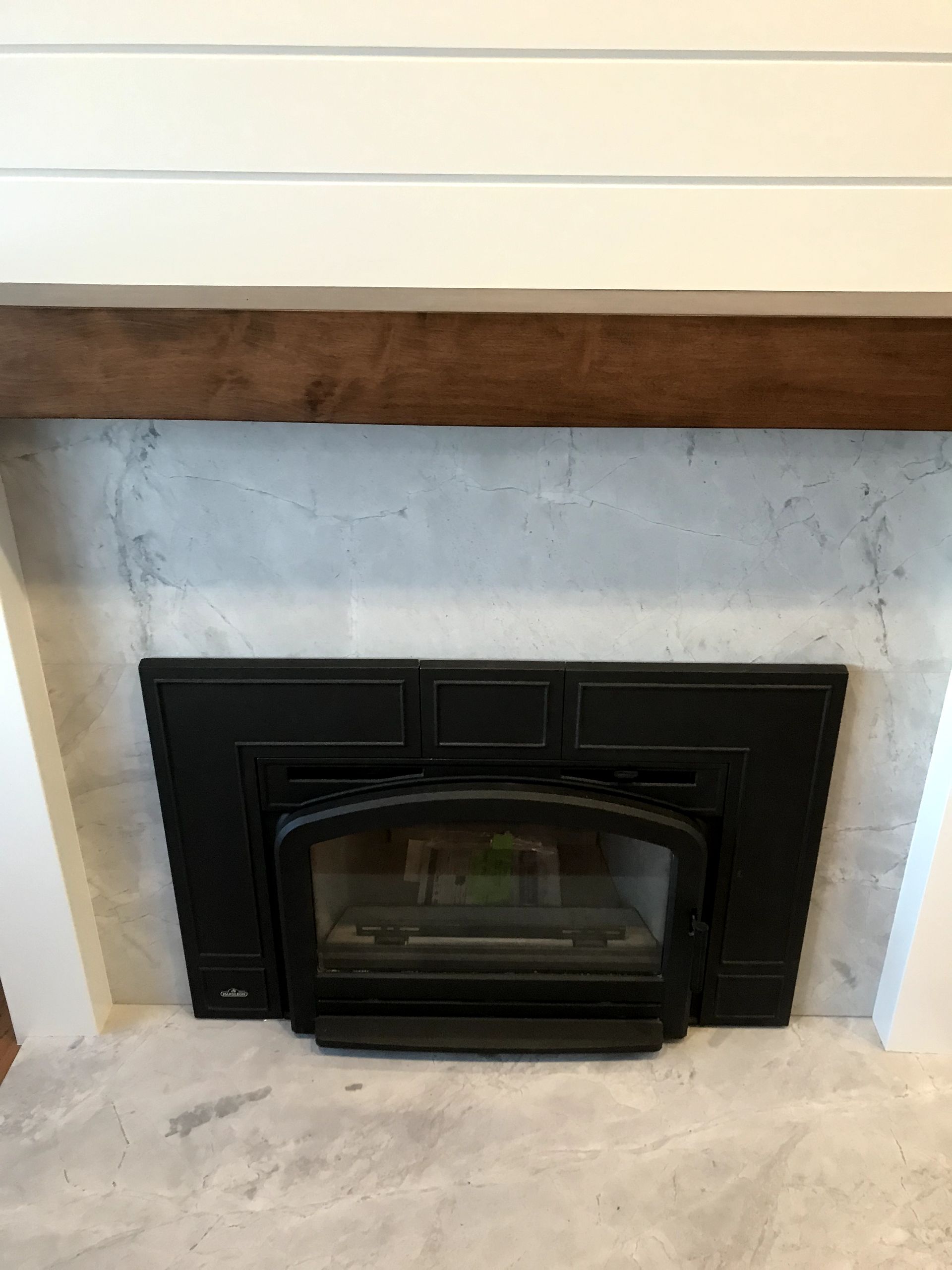 A fireplace with a black insert and a wooden mantle.