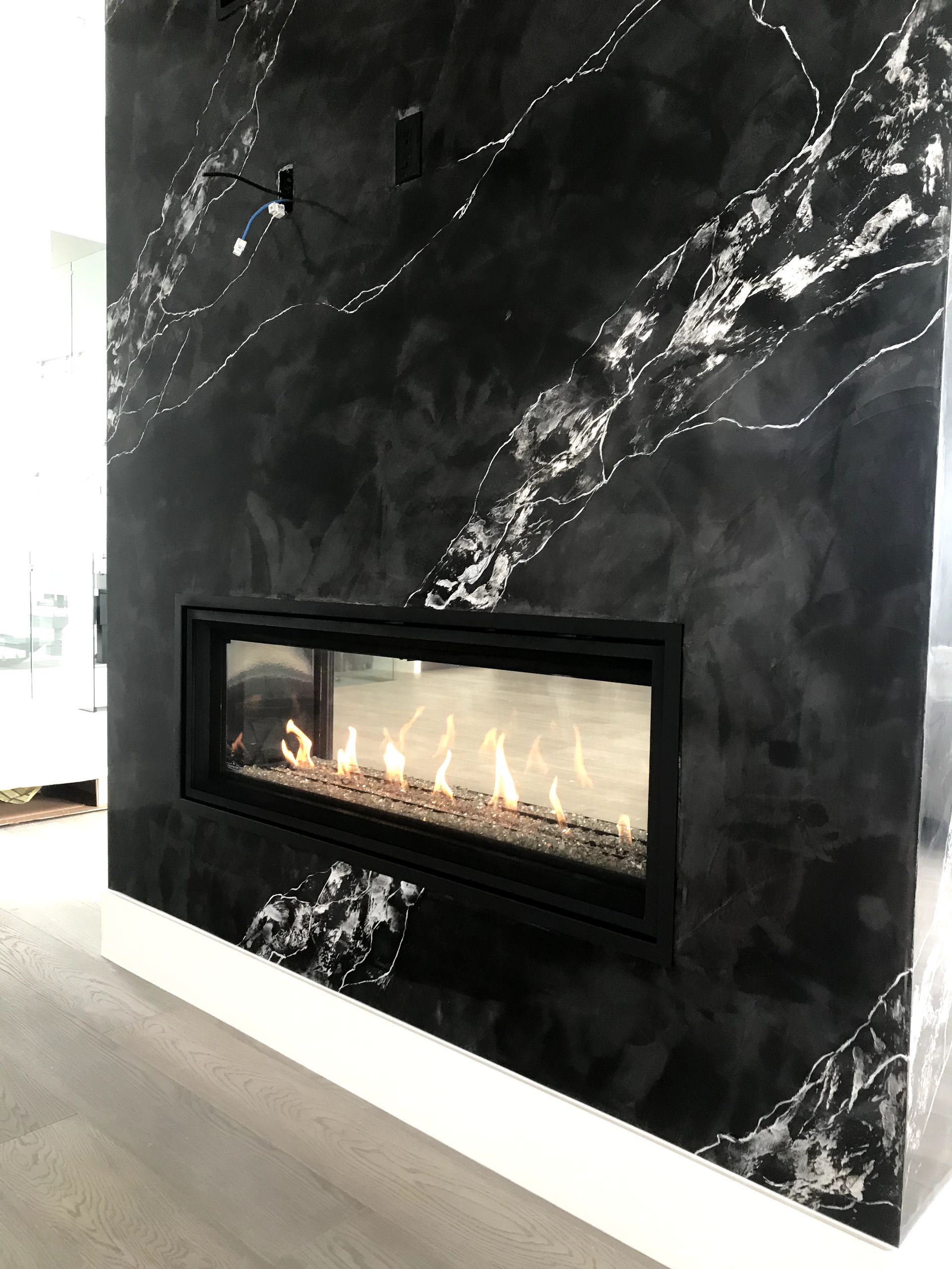 A fireplace is built into a black marble wall in a living room.
