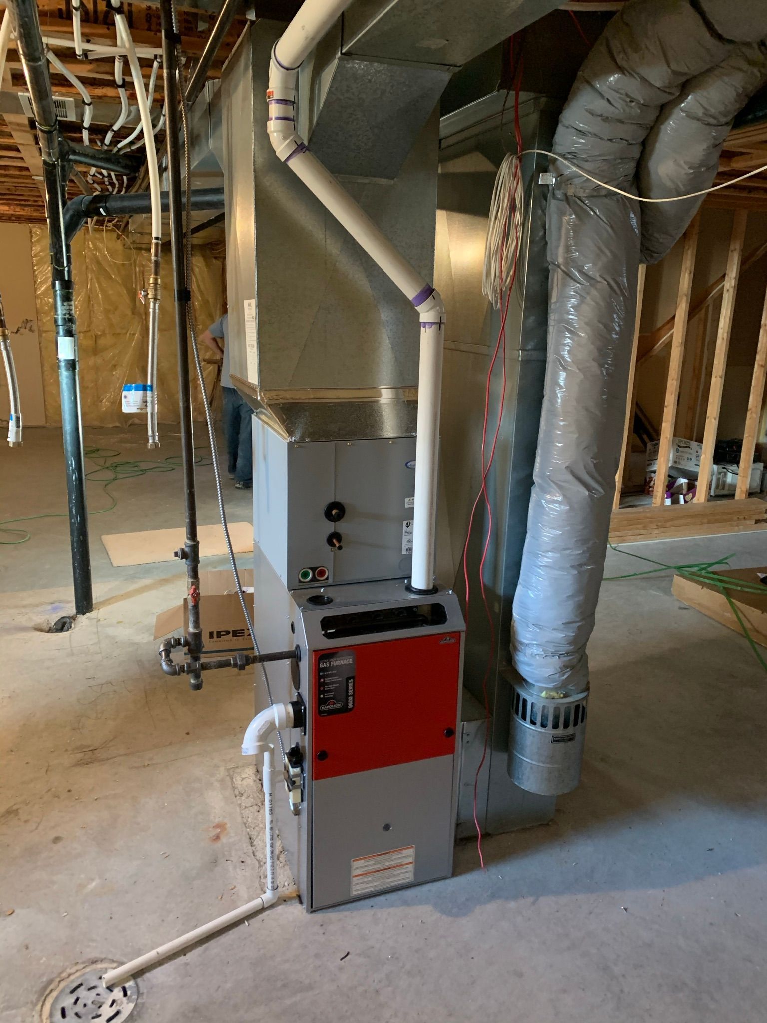 A red and white furnace is sitting in a basement under construction.
