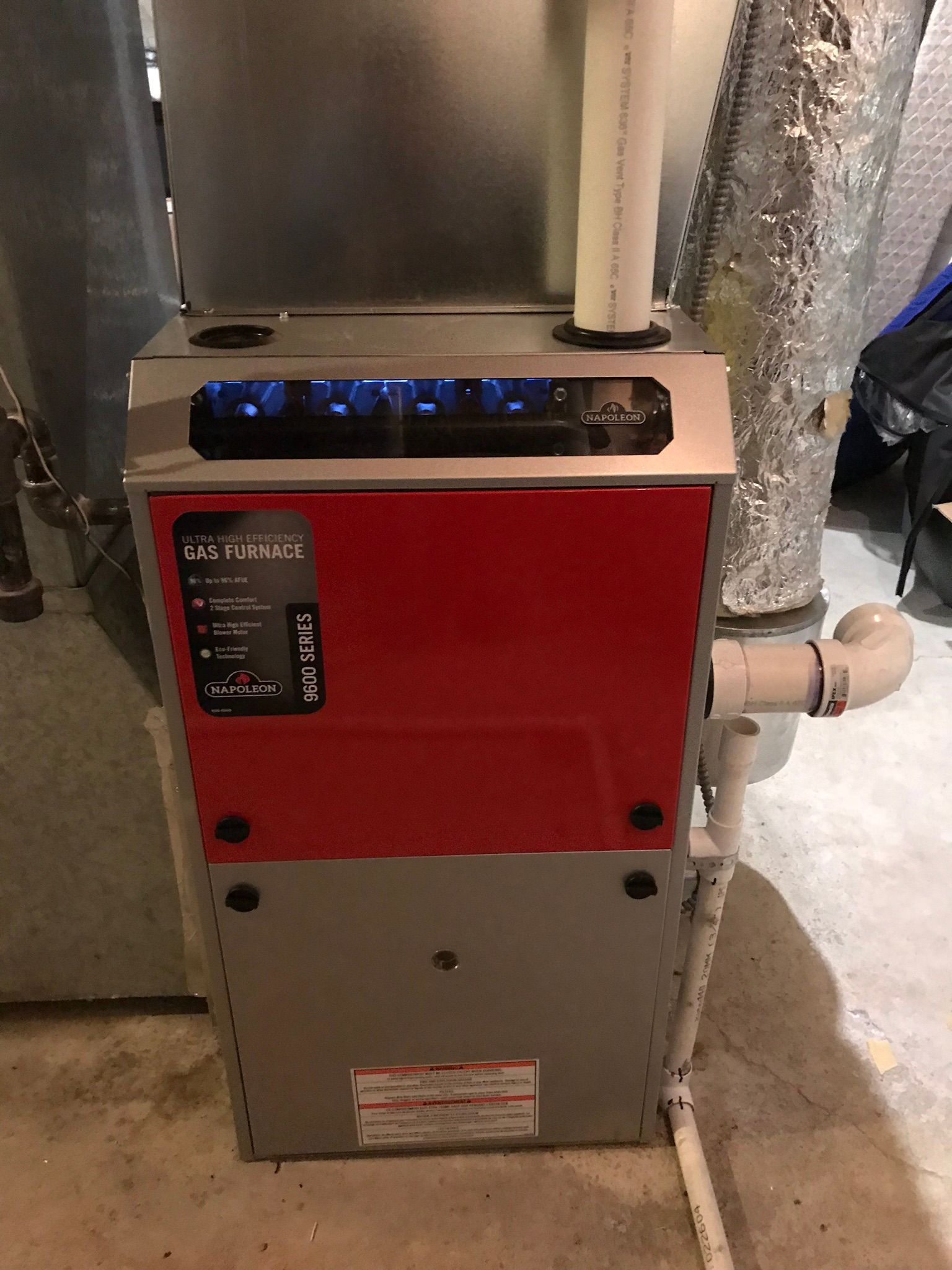 A red and silver furnace is sitting on the floor in a basement.
