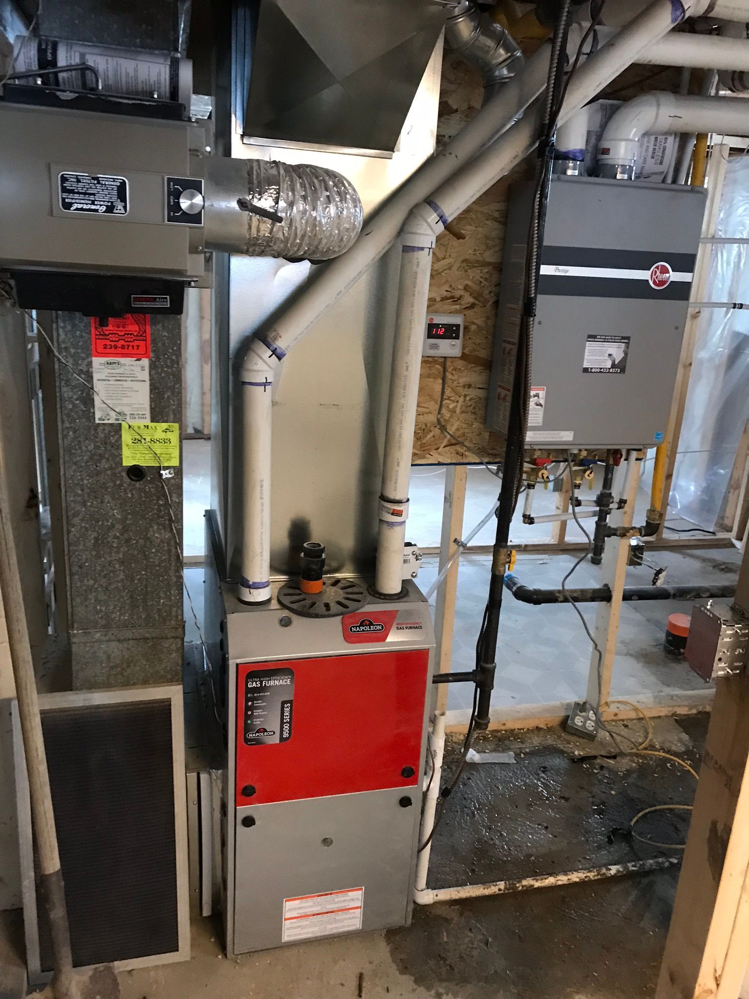 A red and white furnace is sitting in a basement next to a heater.