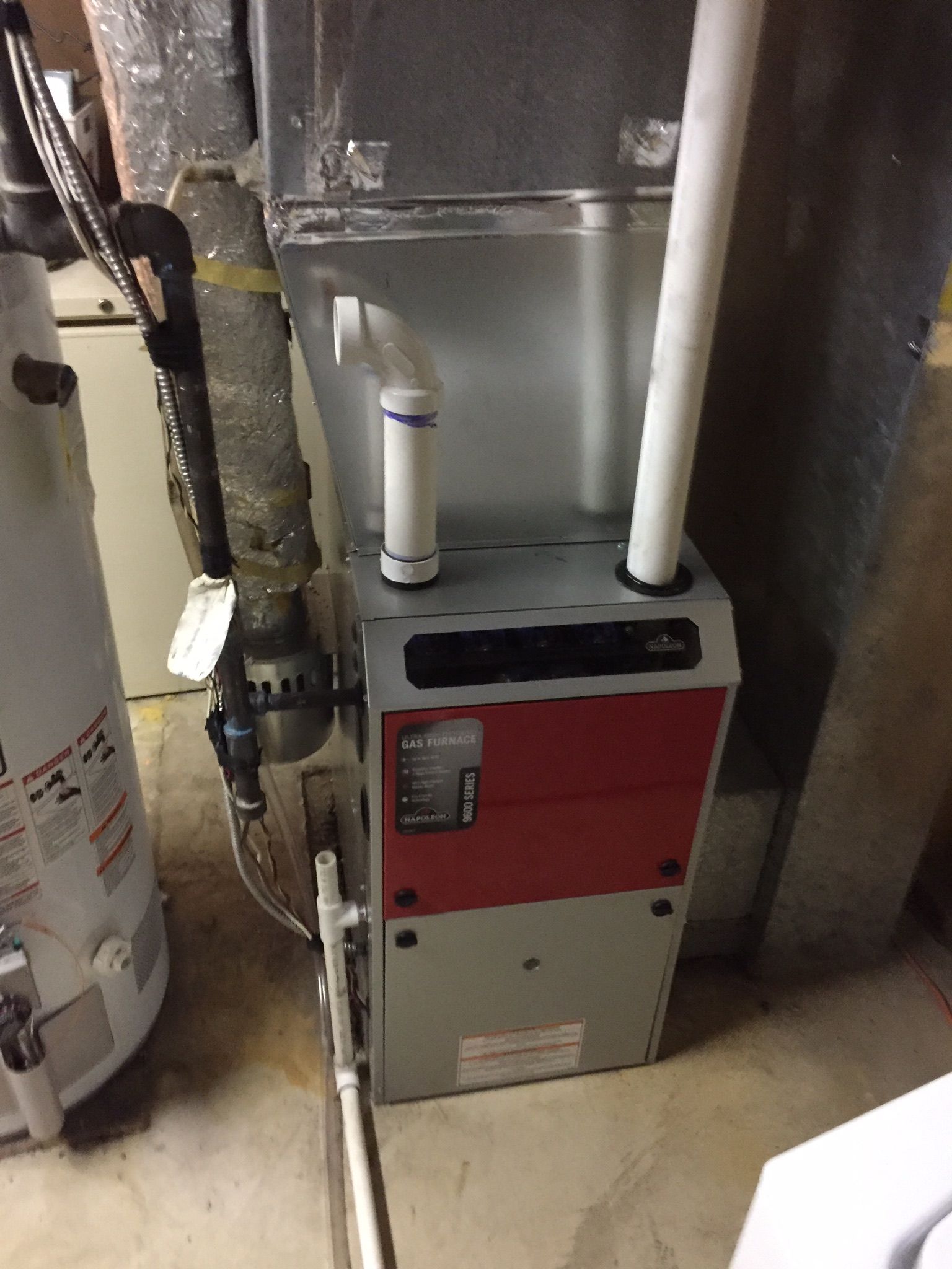 A red and white furnace is sitting in a basement next to a water heater.