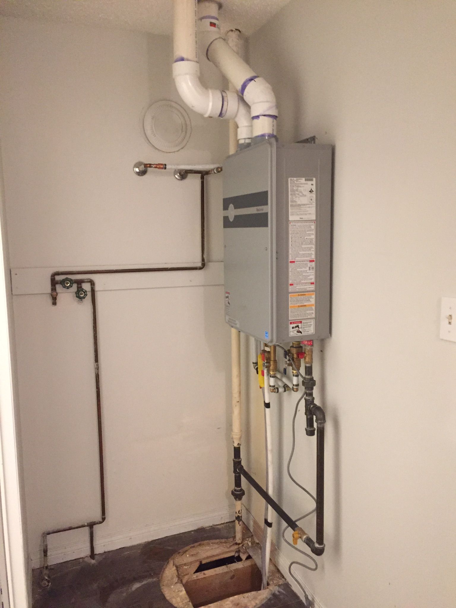 A room with a water heater and pipes on the wall.