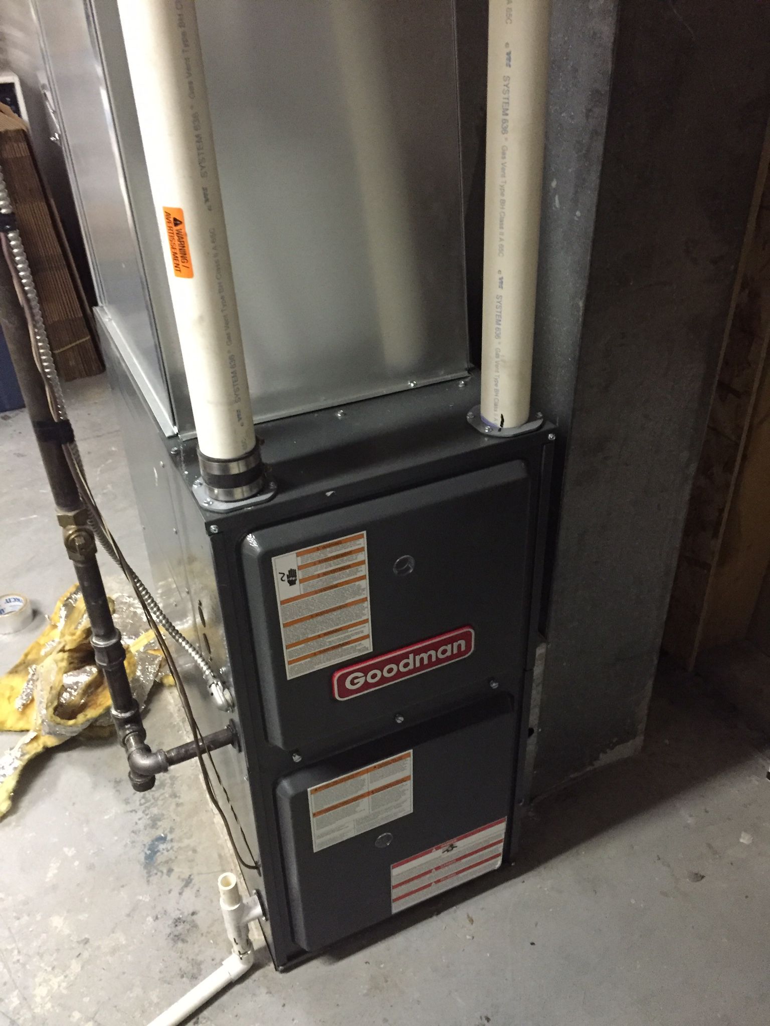 A gas furnace is sitting in a basement next to a wall.