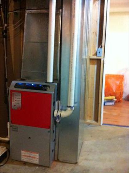 A red and silver furnace is sitting in a basement next to a door.