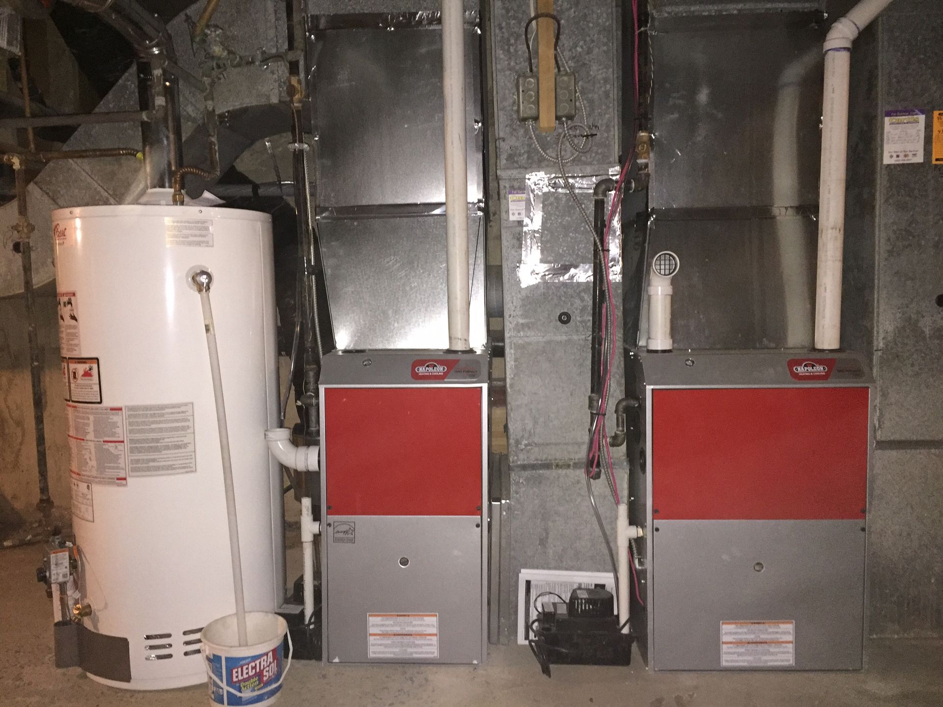 A water heater and a gas heater are sitting next to each other in a basement.