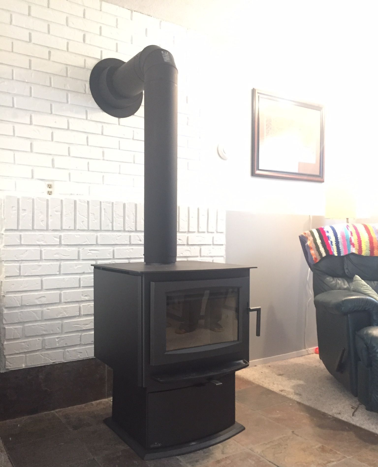 A black wood stove is sitting in a living room next to a white brick wall.