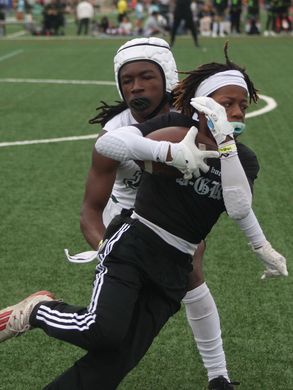 Two young football players in action on a green field. One runs with the ball while the other attempts to tackle him.